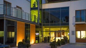 Un hotel moderno con fachada de vidrio, zona de estar al aire libre y un BMW estacionado frente a él.