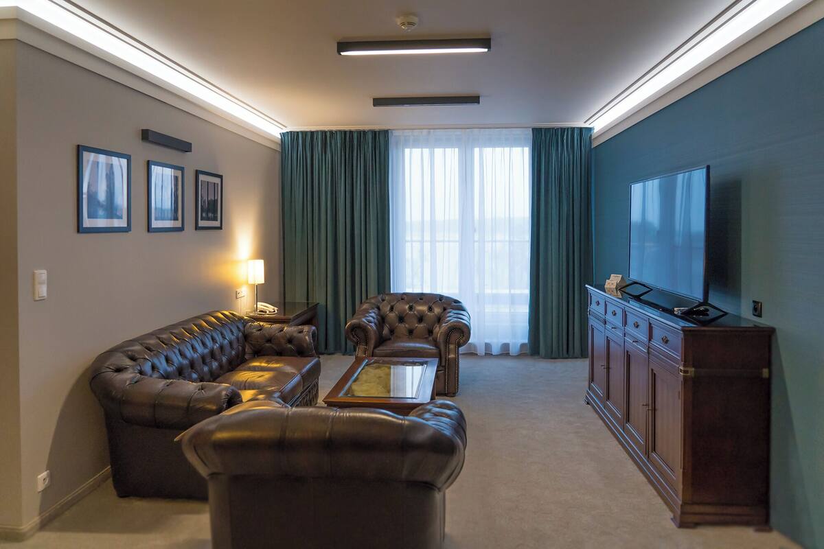 A living room with a sofa, armchair, and ottoman, a television, and a cabinet.
