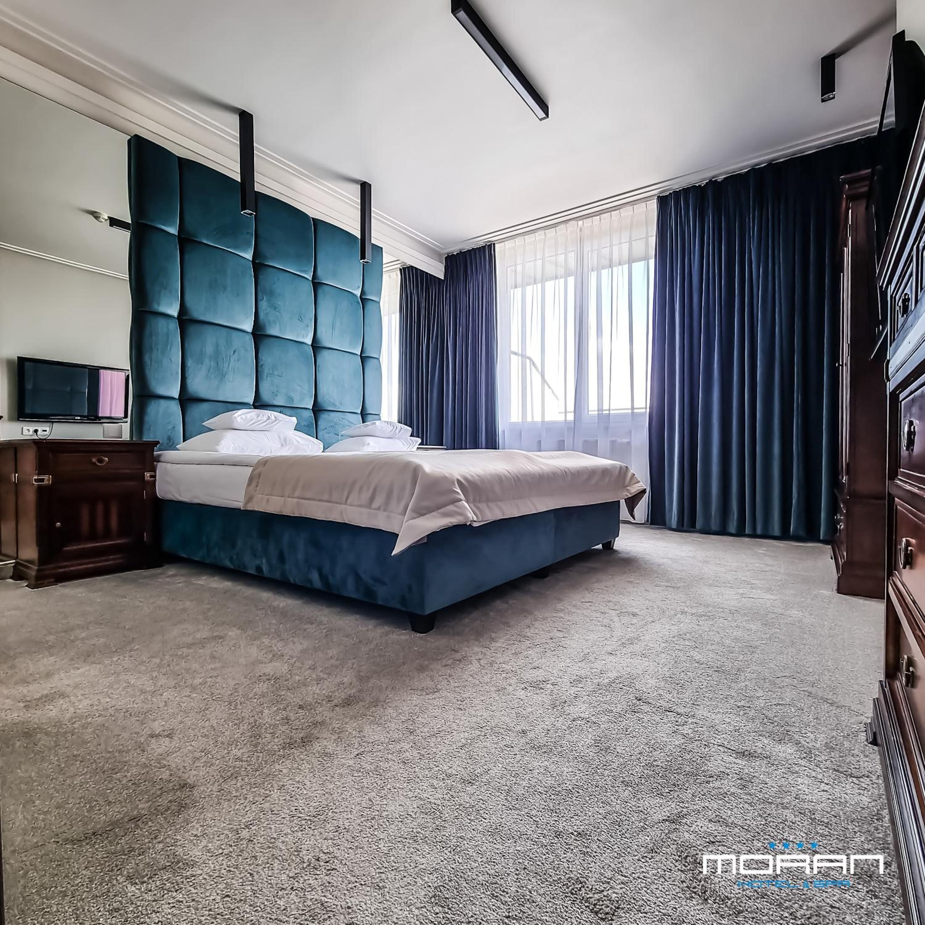 A bedroom with a large bed, a dresser, a television, and a window with curtains.