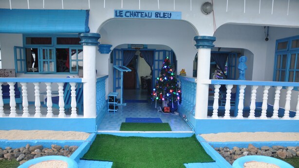 A hotel entrance with a blue and white facade, a Christmas tree, and a sign reading "LE CHATEAU BLEU". - Le Chateau Bleu (Mahé Island)