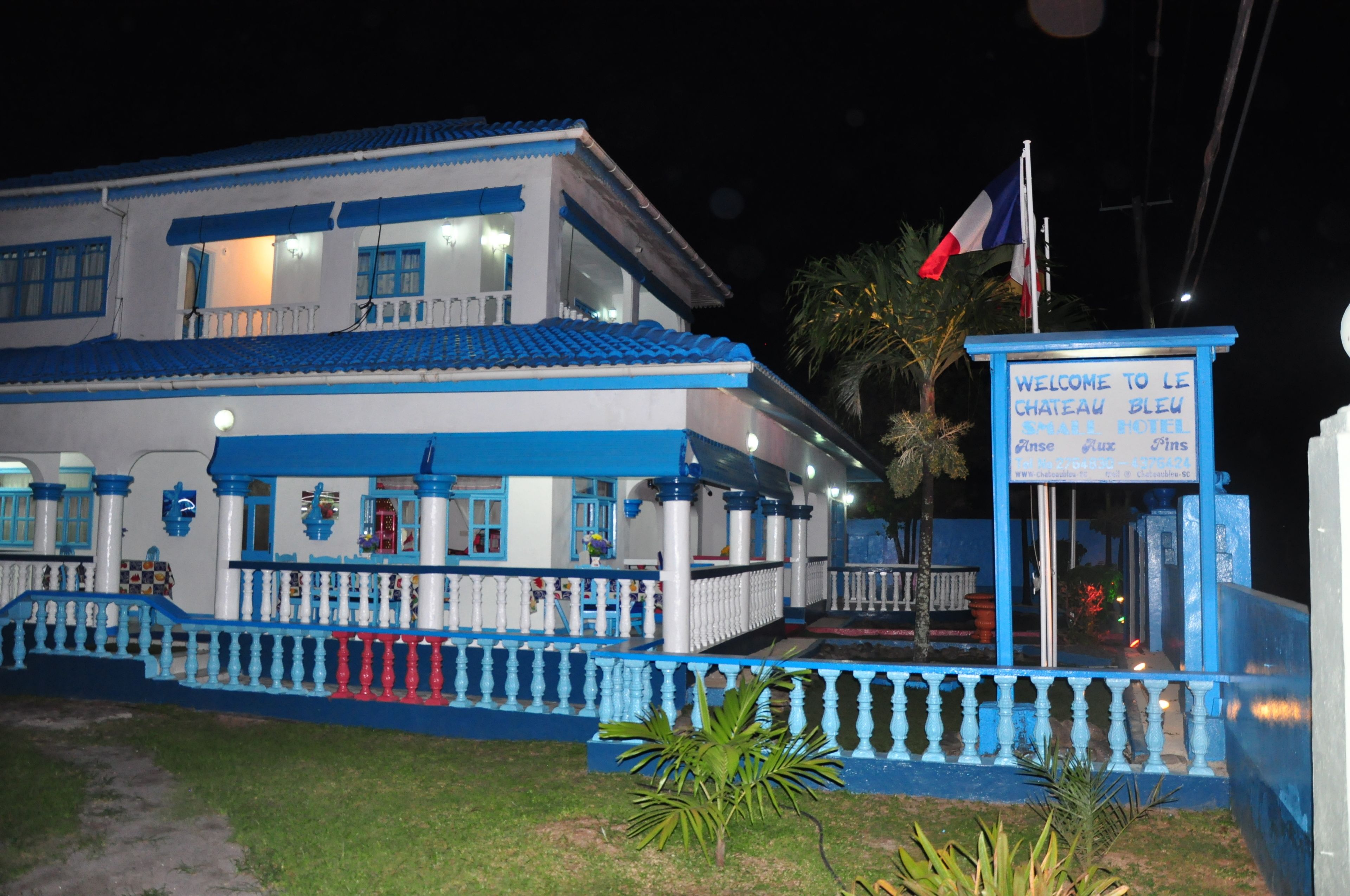 Un hotel amb façana blava i blanca, un rètol amb el nom de l'hotel i una bandera.