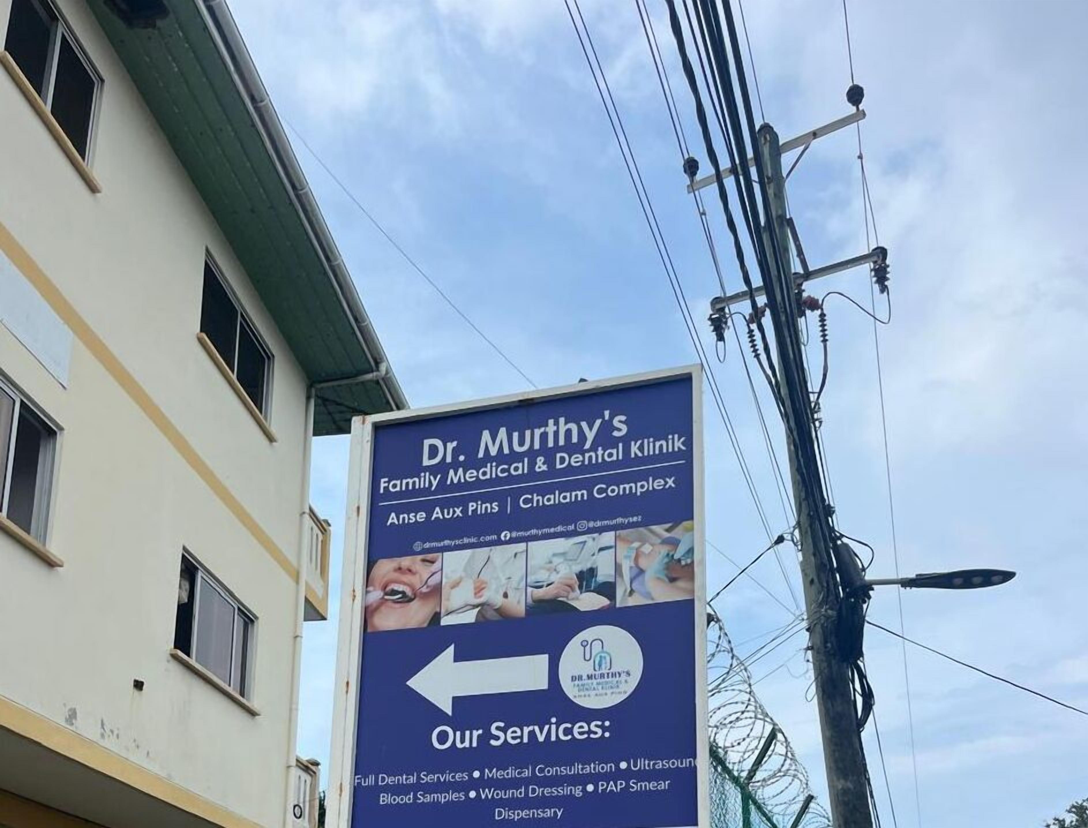 Señal para la Clínica Médica y Dental Familiar del Dr. Murthy, con una lista de servicios que incluye atención dental completa, consulta médica, ecografía, toma de muestras de sangre, curación de heridas, citología vaginal y farmacia.