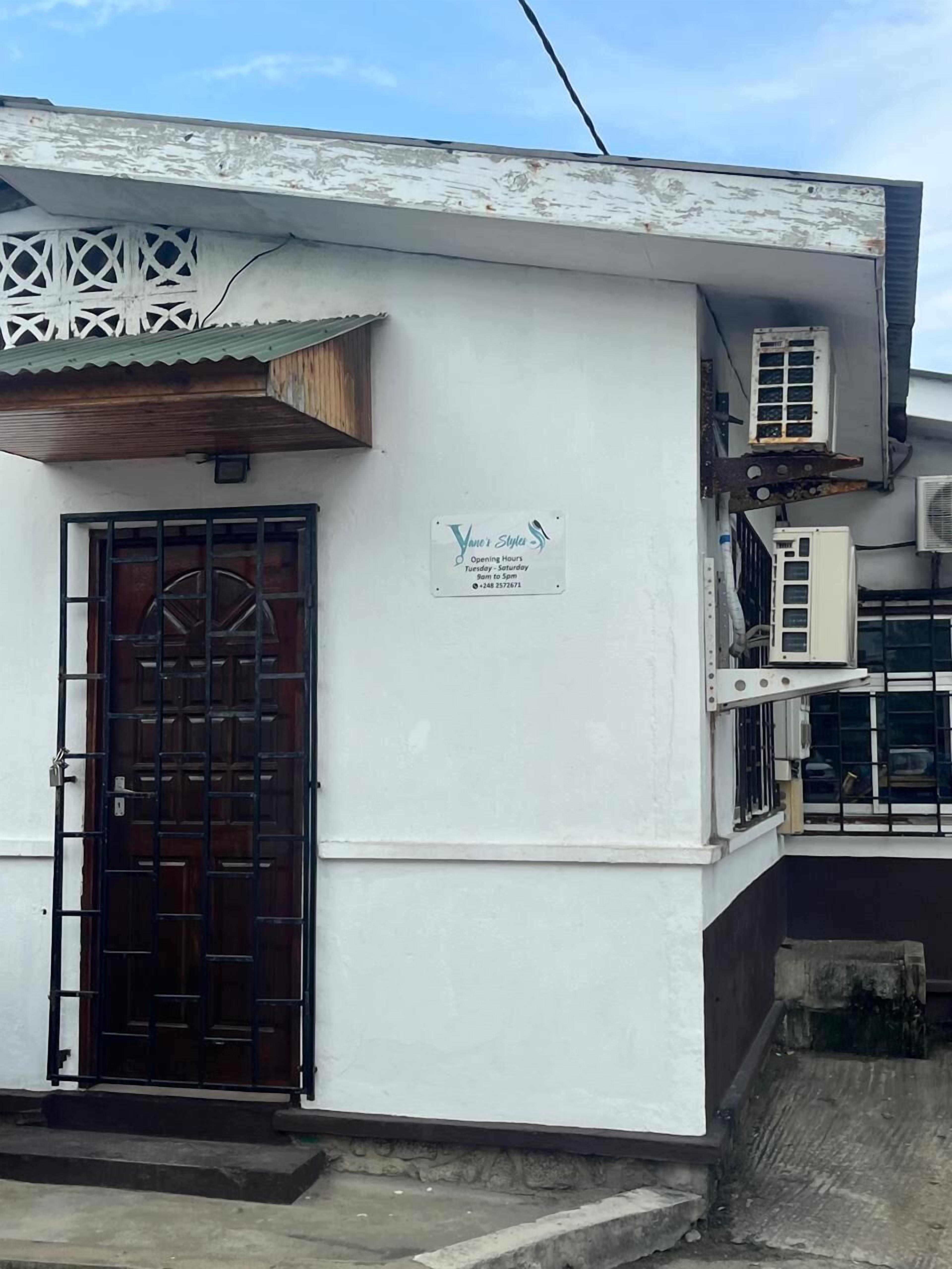 Un edificio con un letrero que indica 'Yane's Styles' y el horario de atención.