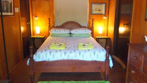 Una cama con dosel de madera, un tapete verde, dos mesitas de noche con lámparas y un aparador de madera.