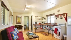 Un espacio habitable compacto con sofá, mesa de centro, cocina con estufa, microondas y estanterías, además de comedor con mesa y sillas.