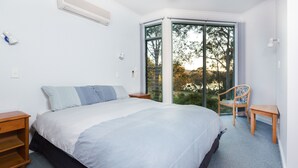 A bedroom with a large bed, a chair, a nightstand, and a window with a view of trees. - Gipsy Point Lodge (Gipsy Point)