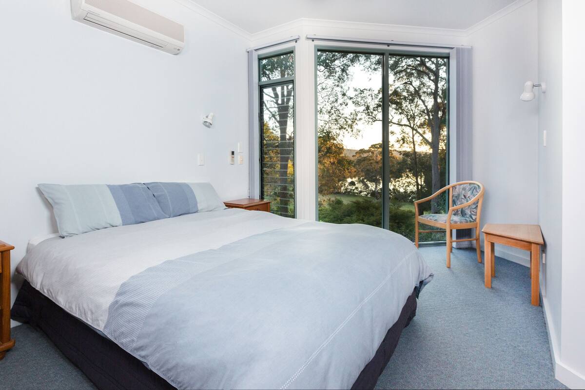 A bedroom with a large bed, a chair, a nightstand, and a window with a view of trees.