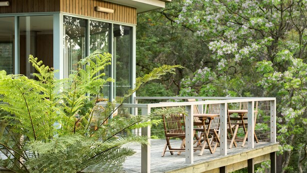 A modern house with a glass facade, wooden deck, and outdoor seating area. - Gipsy Point Lodge (Gipsy Point)