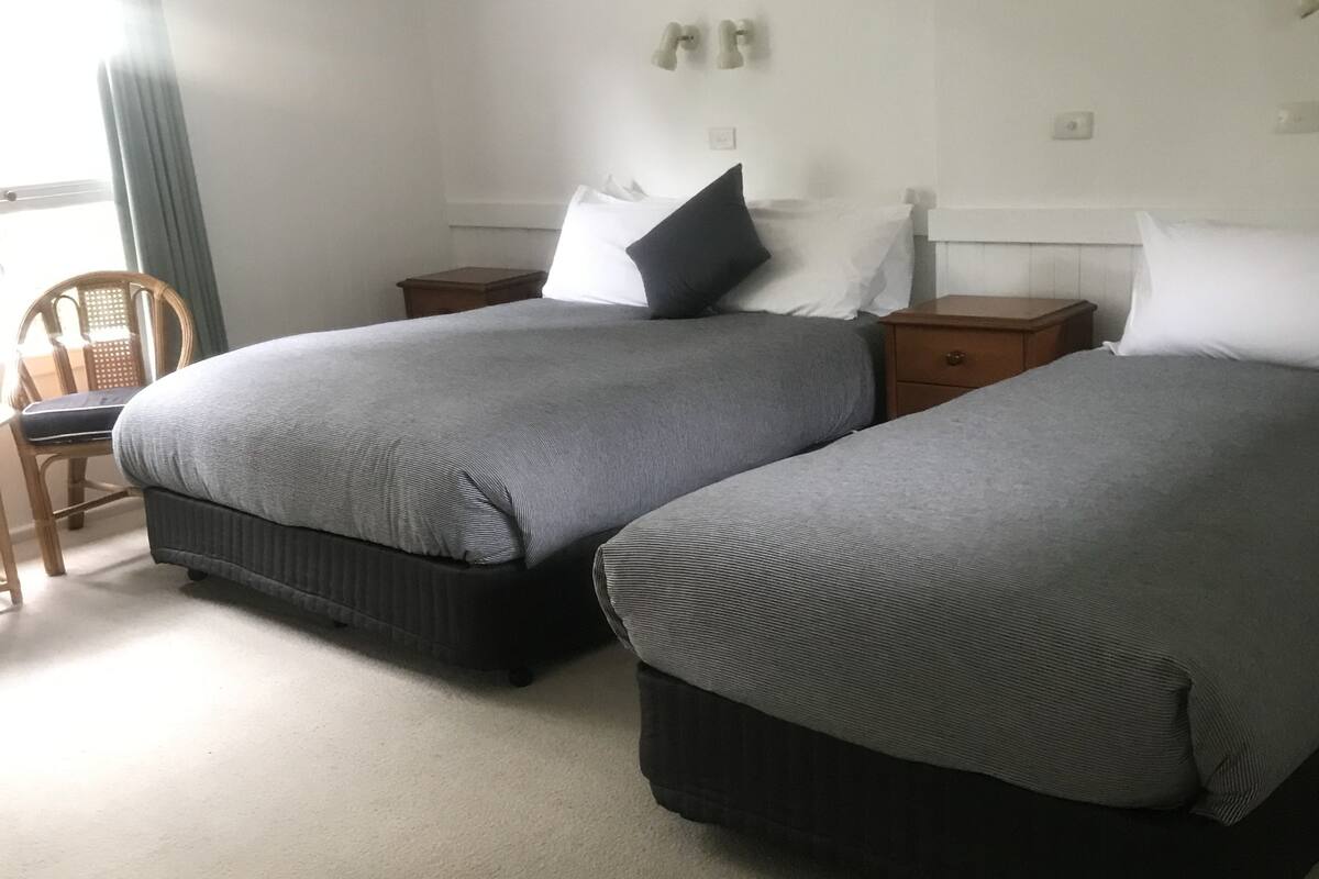 A hotel room with two beds, a wooden chair, and a small table.