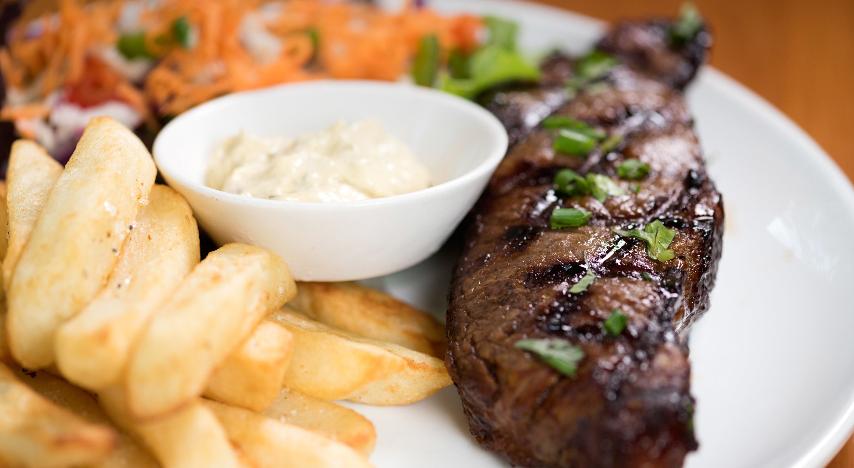 En tallerken med grillet bøf, pommes frites og en salat.