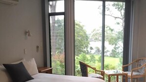 A bedroom with a large bed, a ceiling fan, and a view of the outdoors through large windows.