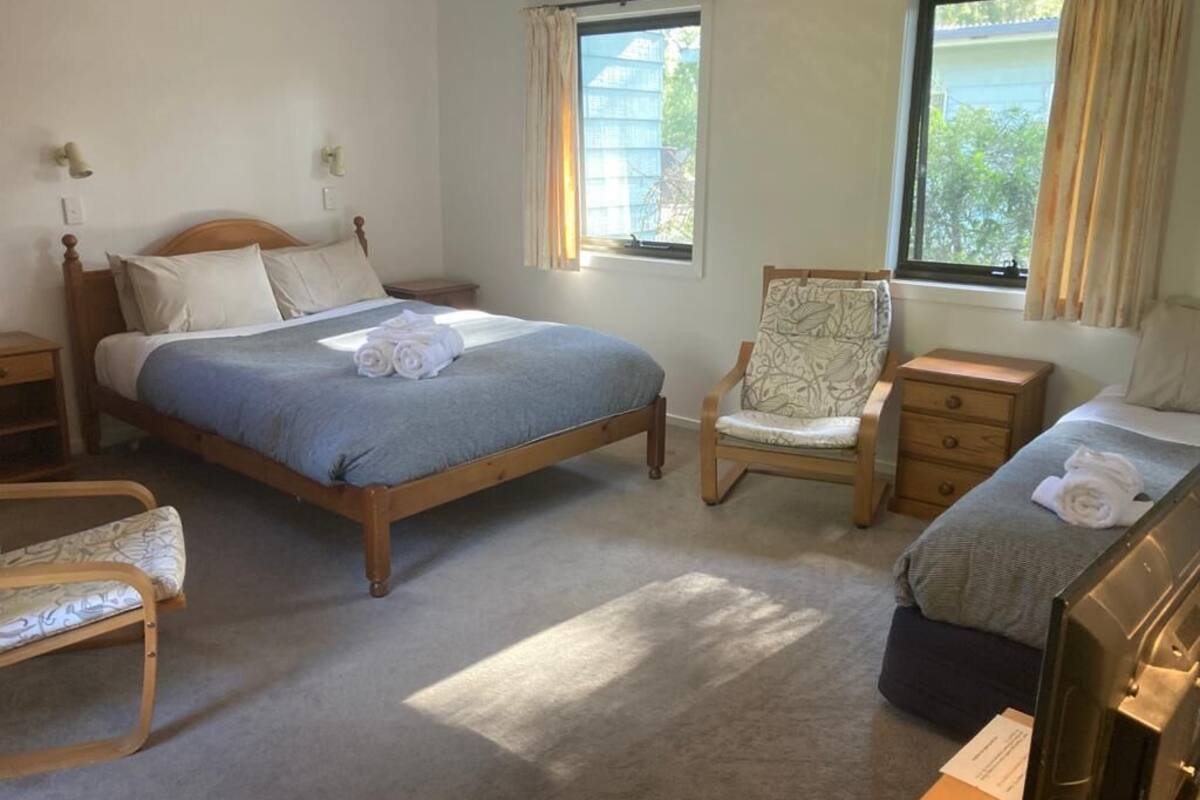 A bedroom with a large bed, a chair, a desk, and two windows.