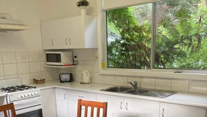 A kitchen with white cabinets, a stove, a microwave, and a sink. There is a window with a view of greenery outside. - Gipsy Point Lodge (Gipsy Point)