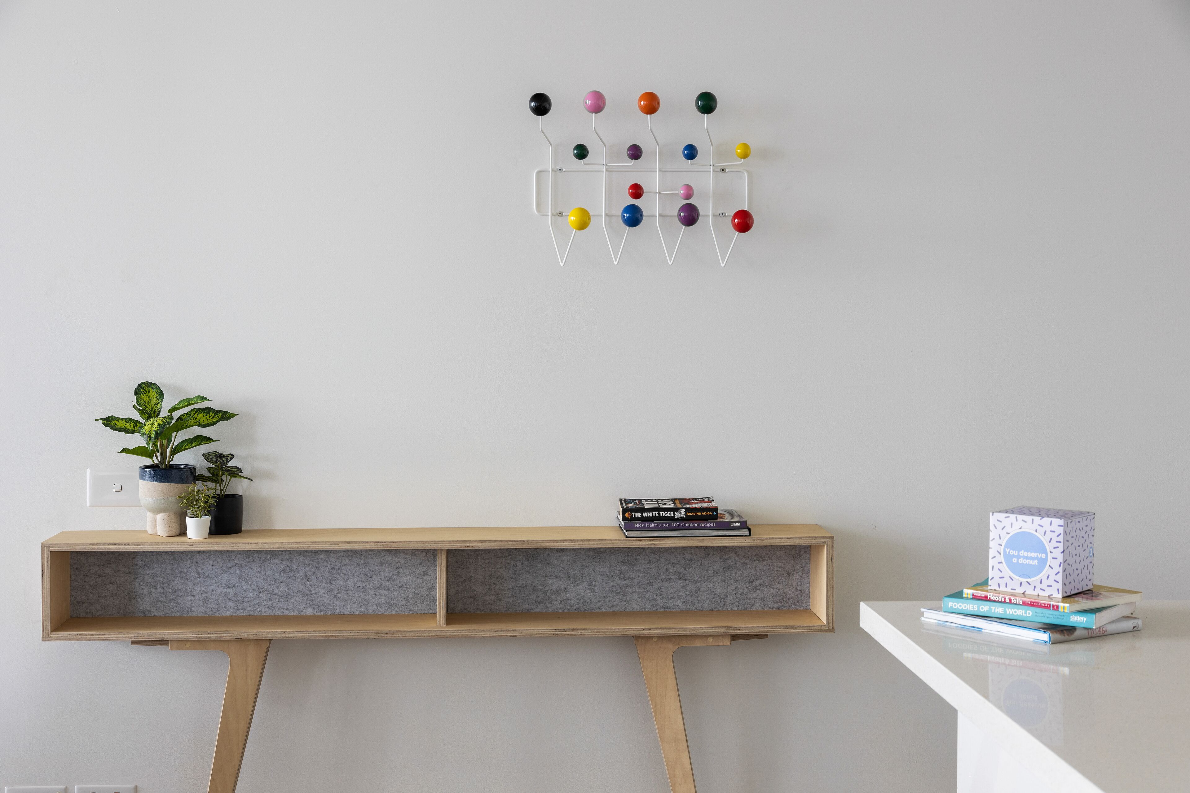 A minimalist room with a wooden desk, a wall-mounted color ball hook organizer, a small potted plant, and a stack of books.