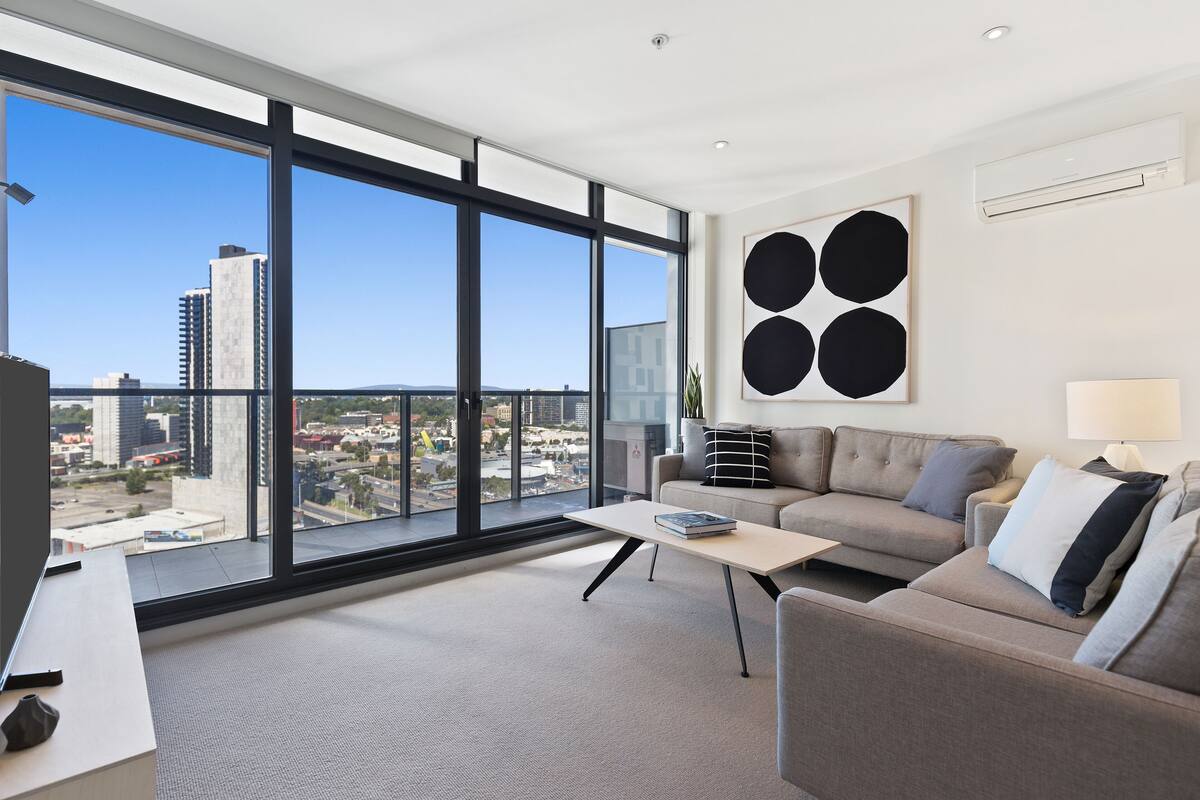 A modern living room with a large window, a sofa, a coffee table, and a minimalist art piece on the wall.