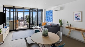 Een moderne woonkamer met een groot raam, een grijze bank, een ronde tafel en uitzicht op de stad.