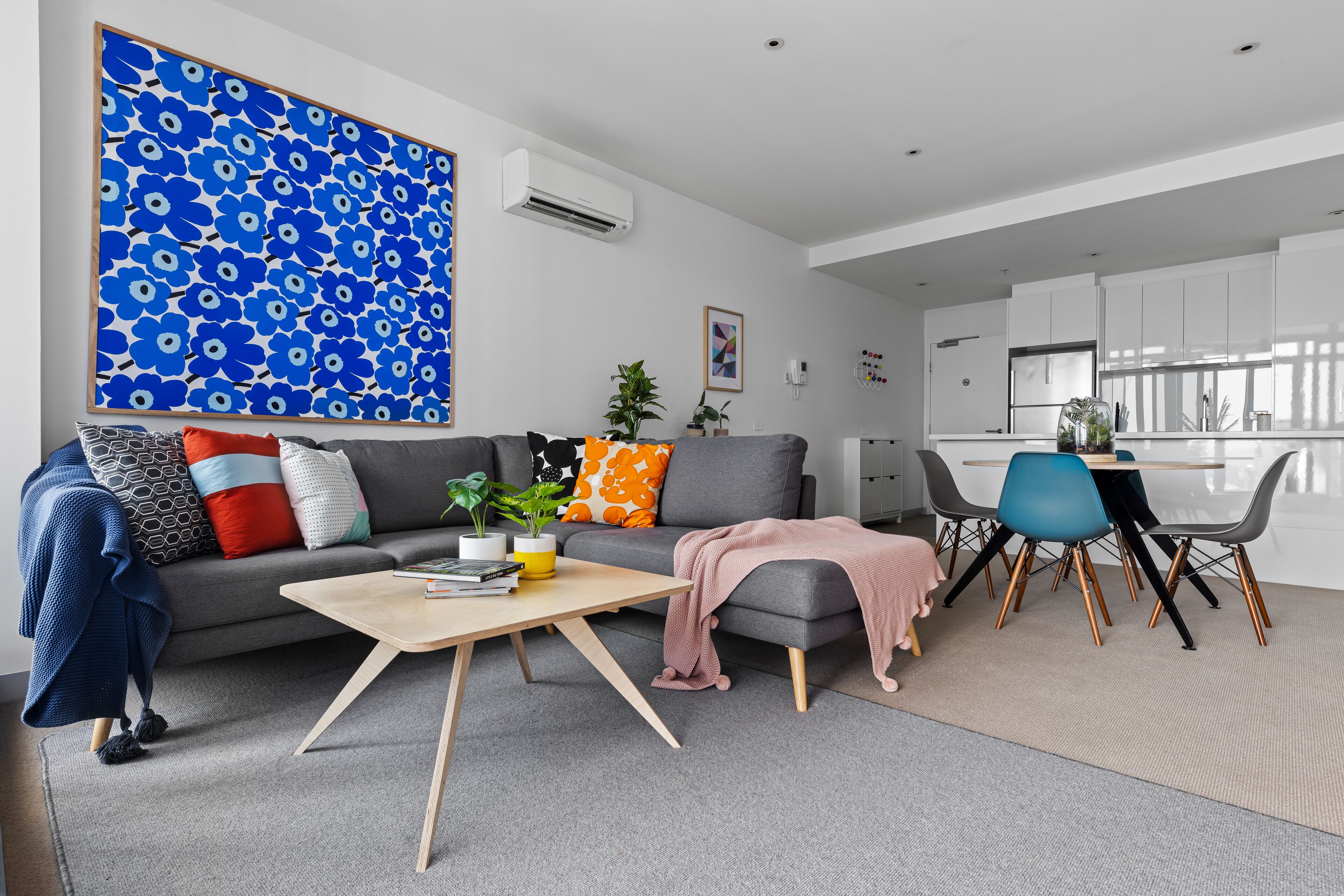 A modern living room with a grey sofa, a coffee table, and a dining area with a blue chair.