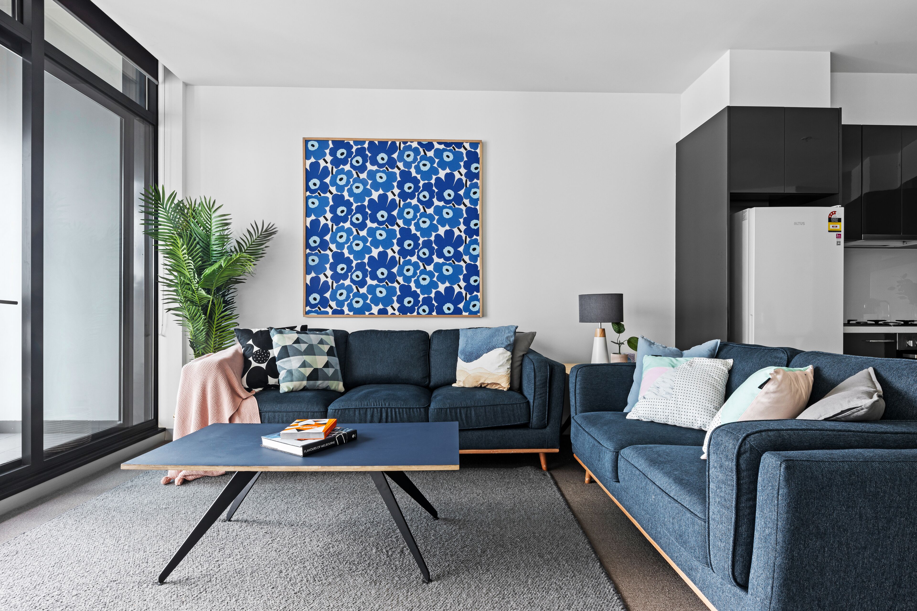 A modern living room with a dark blue sofa, a coffee table, and a large blue floral artwork on the wall.