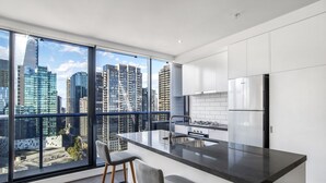 Een moderne keuken met een groot eiland, roestvrijstalen apparatuur en een stadsgezicht door het plafondhoge raam.