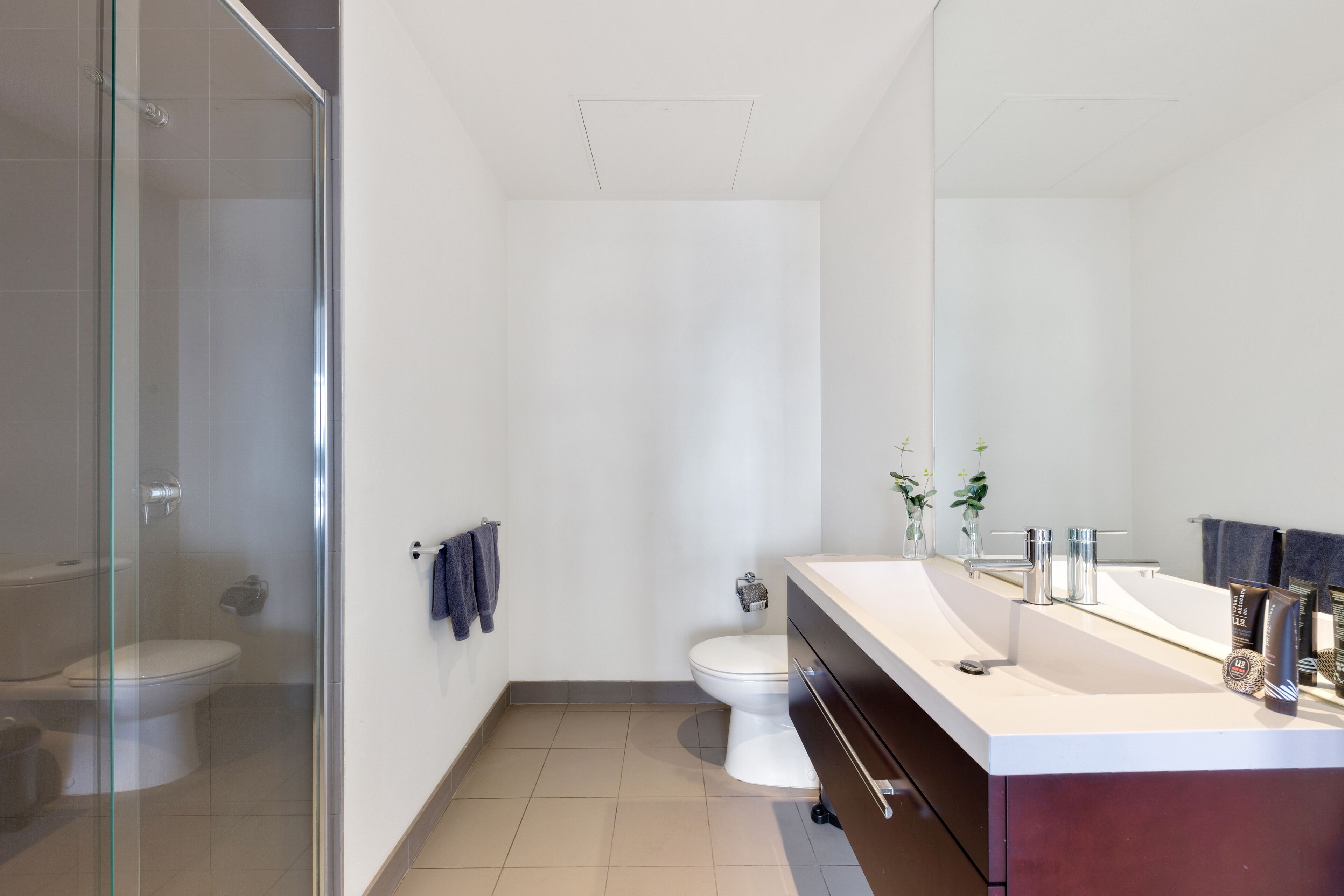 Une salle de bain moderne avec une douche à parois de verre, des toilettes blanches, un meuble-lavabo avec un miroir et un évier.