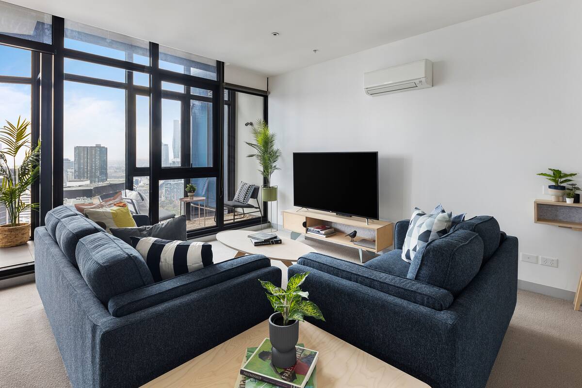 A modern living room with a large window, a flat-screen TV, and a sofa set.