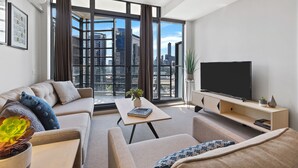 Een moderne woonkamer met een bank, een salontafel, een televisie en een groot raam met uitzicht op de stad.