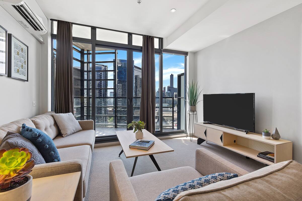 A modern living room with a sofa, a coffee table, a TV, and a large window with a city view.