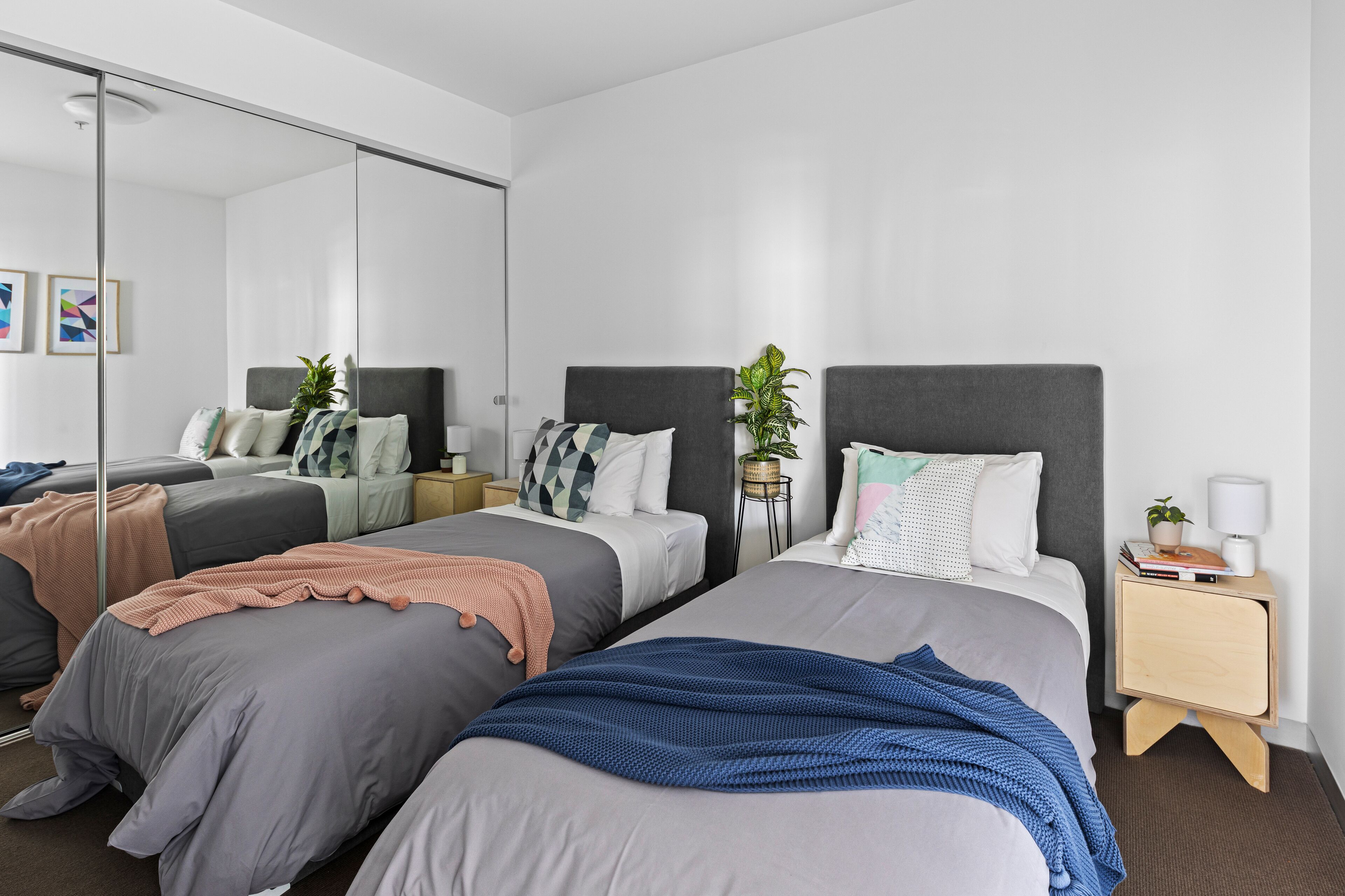 Ein modernes Schlafzimmer mit zwei Betten, einem Nachttisch mit Lampe und einem Spiegel.