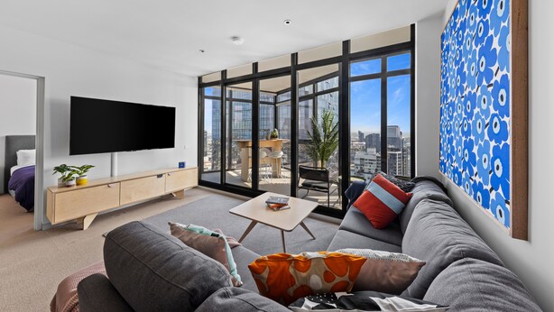 Een moderne woonkamer met een grote televisie, een bank, een salontafel en een balkon met uitzicht op de stad.