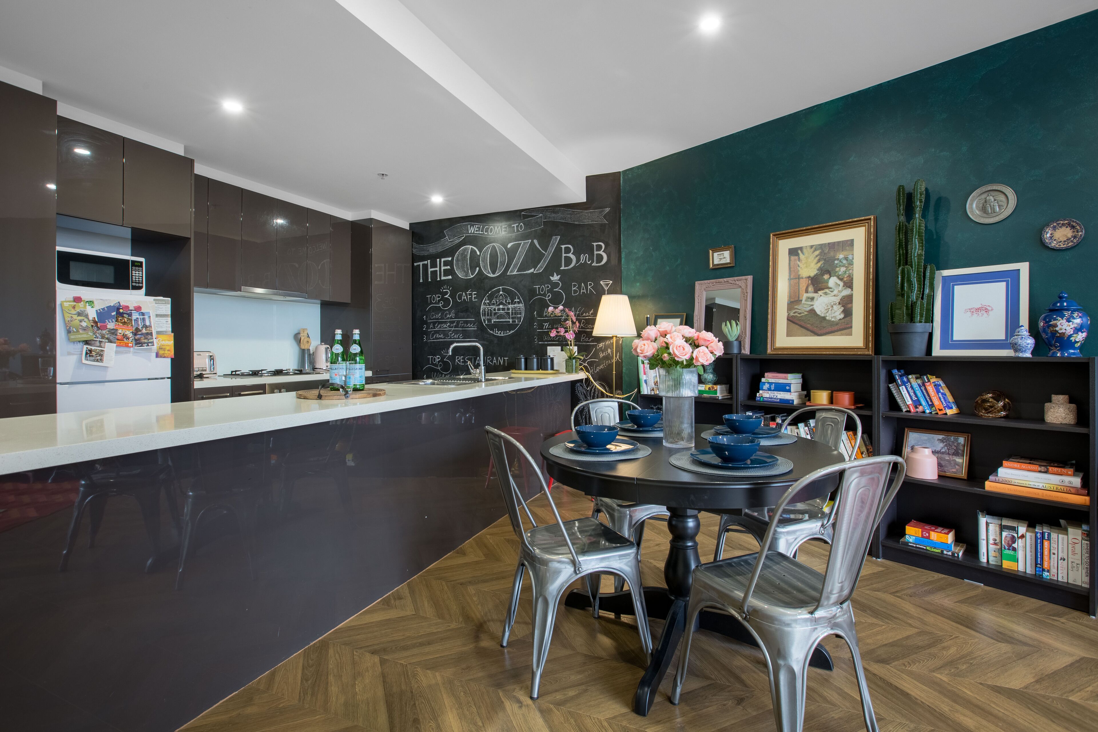 A modern kitchen with a black countertop, stainless steel appliances, and a chalkboard wall with "The Cozy Bar" written on it.