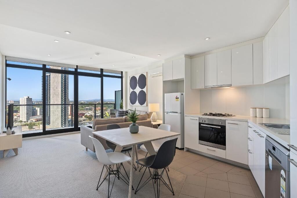 Une cuisine moderne avec des meubles blancs, un coin repas comprenant une table et des chaises, et une grande fenêtre offrant une vue sur la ville.