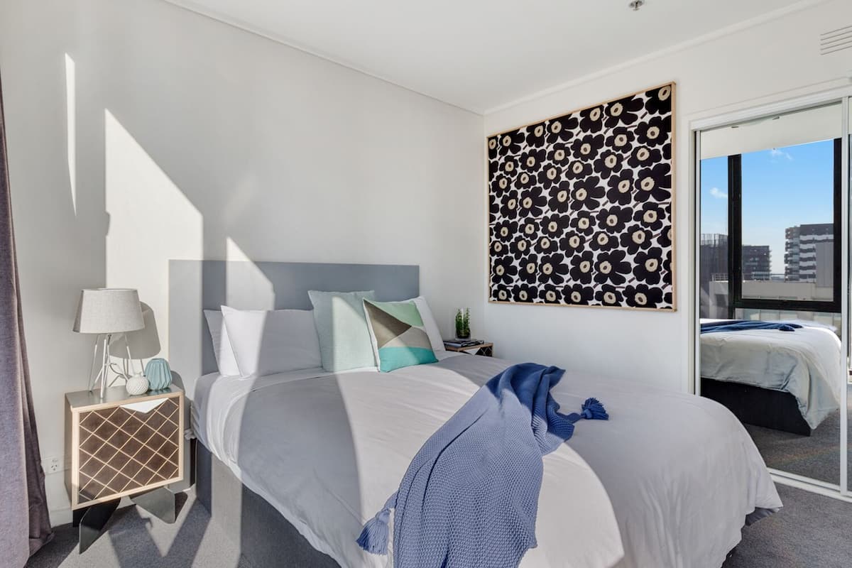 Un dormitorio moderno con una cama grande, una mesita de noche con lámpara, una obra de arte en la pared y vistas amplias a través de un ventanal.