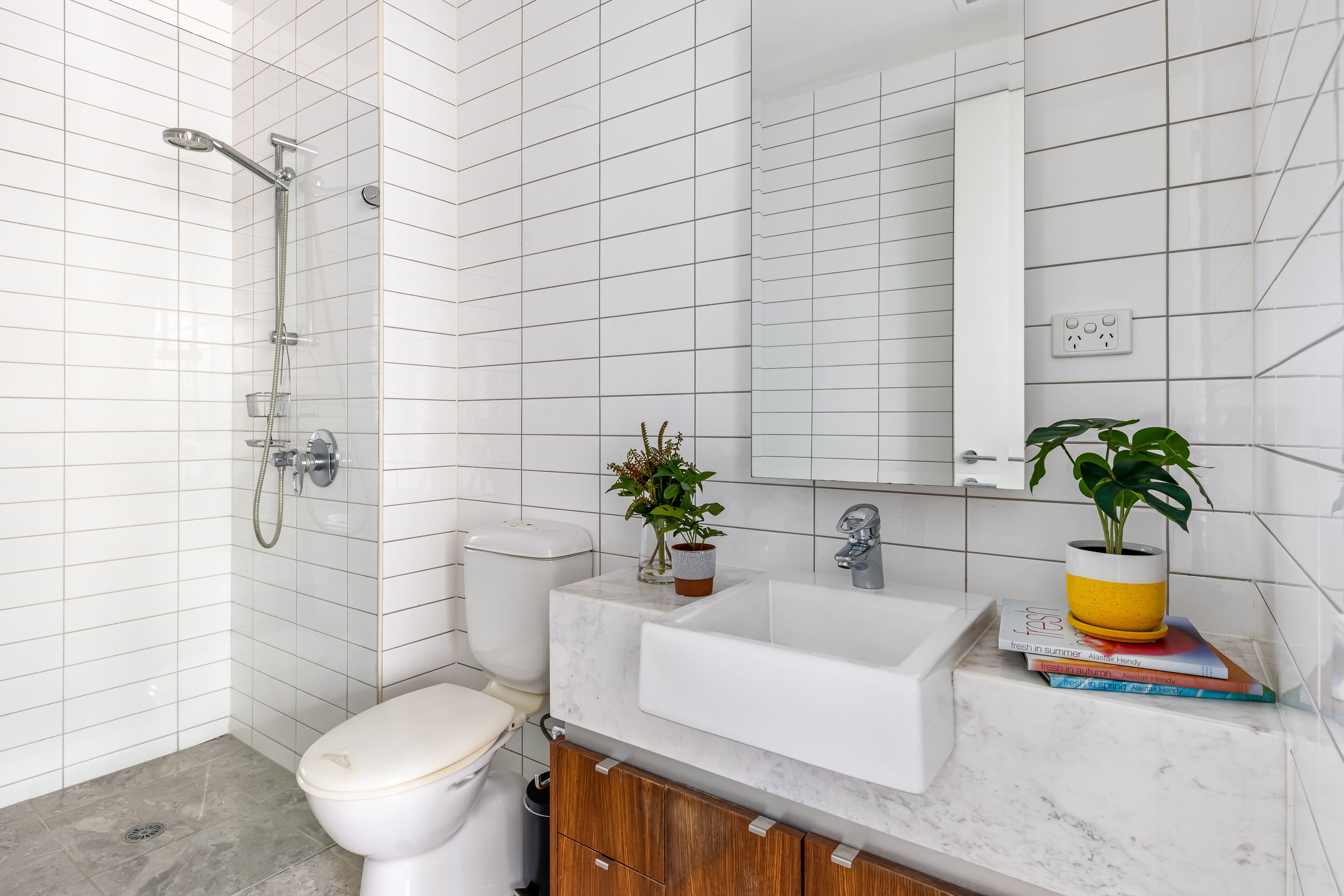 Een moderne badkamer met witte metro tegels, een witte wastafel, een spiegel en een douche.