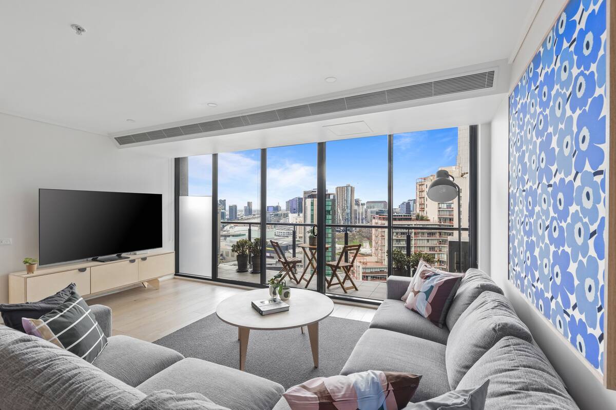 Una sala de estar moderna con un televisor grande, asientos cómodos, una mesa de centro y un balcón con vista a la ciudad.