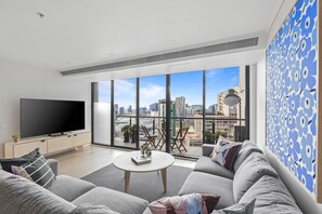 Ein modernes Wohnzimmer mit großem Fernseher, bequemen Sitzmöglichkeiten, einem Couchtisch und einem Balkon mit Blick auf die Stadt.