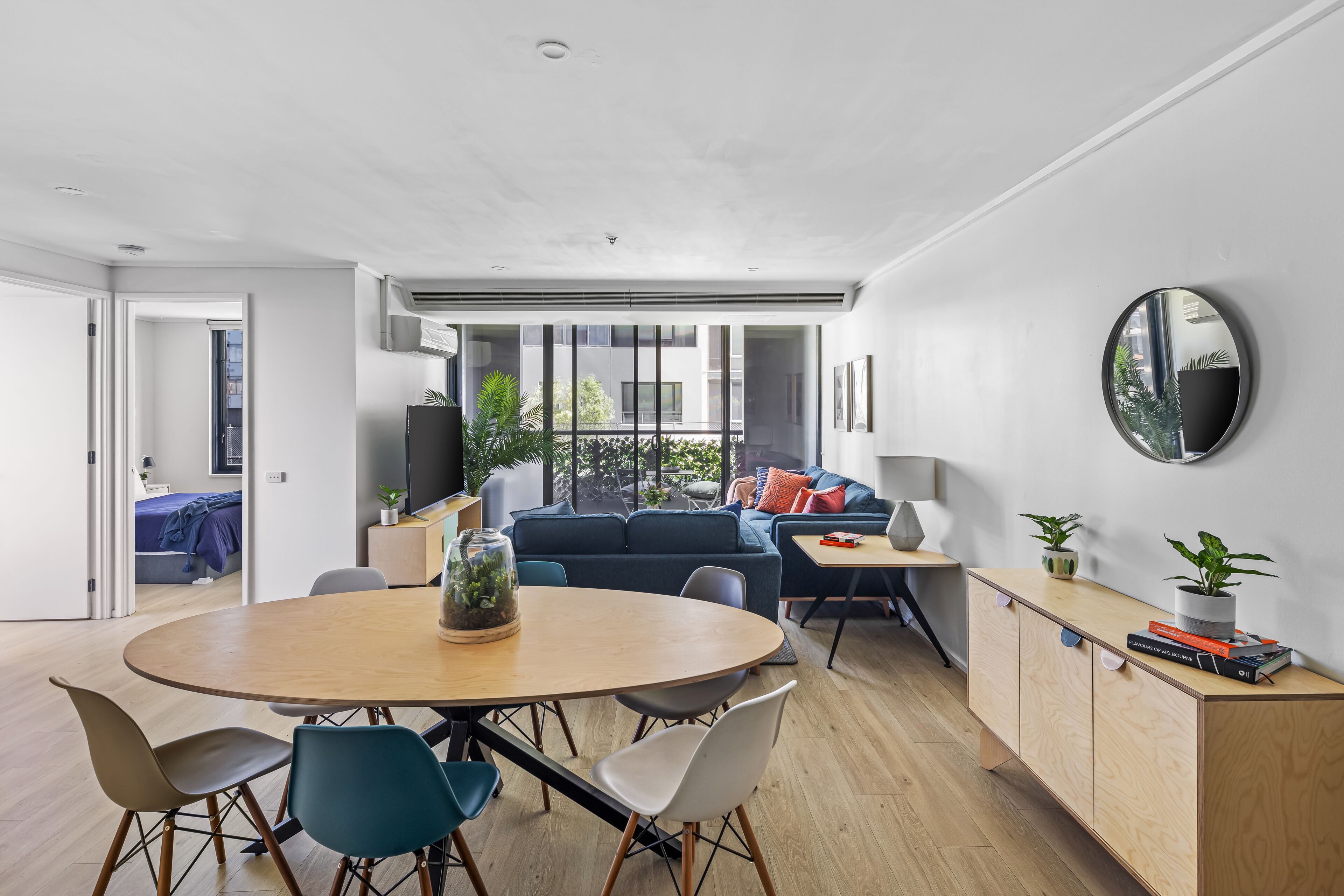 Ein modernes Wohnzimmer mit einem runden Holztisch, einem blauen Sofa und Blick ins Freie durch große Fenster.