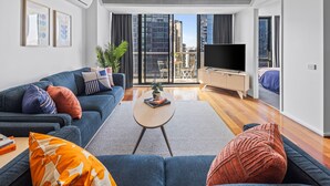 A modern living room with a sofa, coffee table, and TV. There is a balcony with a view of buildings. - Nook Melbourne 173 City Road (Southbank)