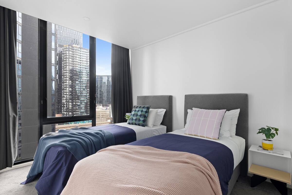 Habitación de hotel moderna con dos camas, un ventanal grande con vista a la ciudad y una mesita de noche con una planta.