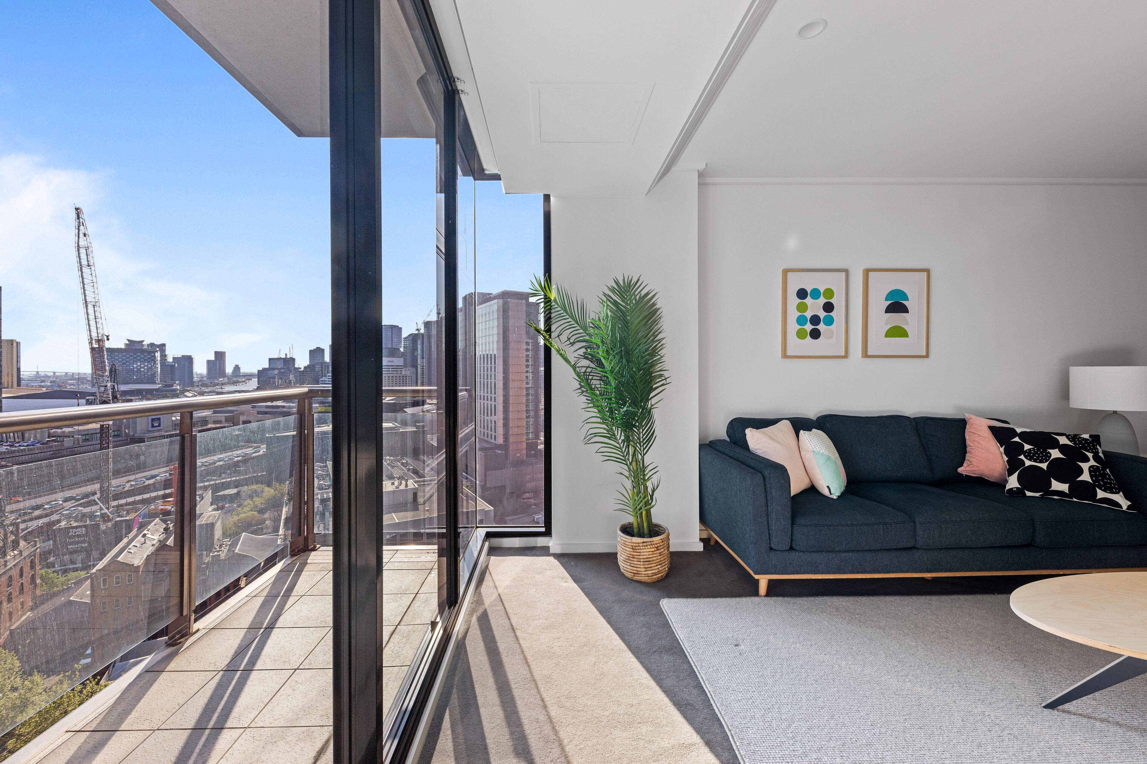 Un salón moderno con balcón y vistas a la ciudad, un sofá oscuro, una mesita y una planta en maceta.