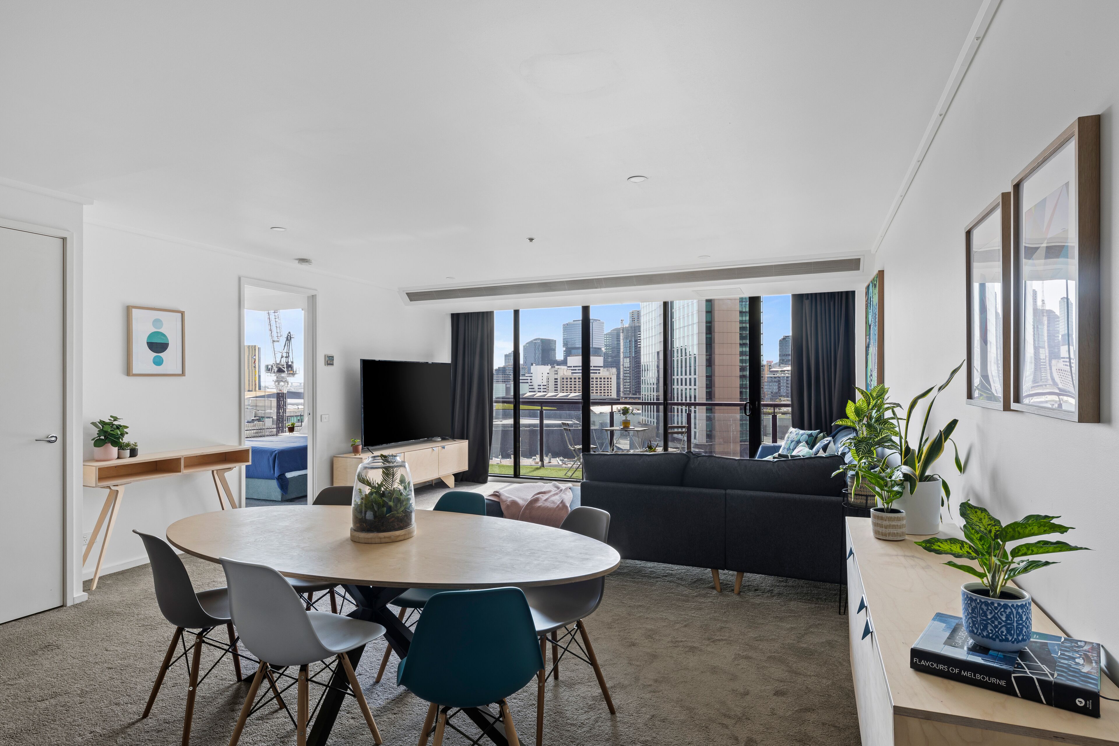 A modern living room with a round table, chairs, a sofa, and a large window with a city view.