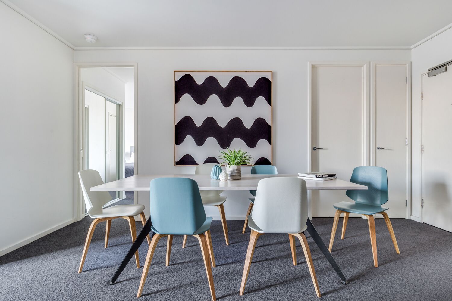 A modern meeting room with a white table, six chairs, and a large abstract painting on the wall.