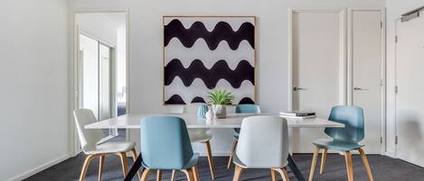 A modern meeting room with a white table, six chairs, and a large abstract painting on the wall.
