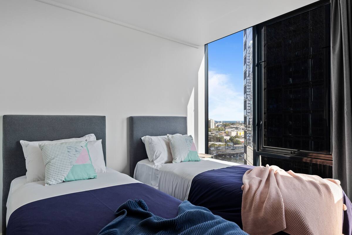 Habitación de hotel con dos camas, un ventanal amplio con vistas a la ciudad y un diseño moderno.