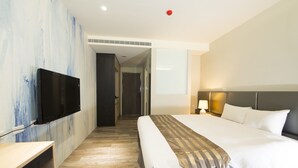 Una habitación de hotel con una cama, un televisor de pantalla plana en la pared, un escritorio y una lámpara.