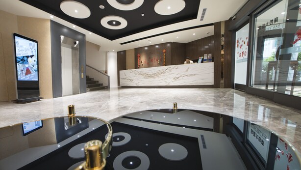 Un moderno vestíbulo de hotel con una recepción de mármol, una pantalla digital y una escalera que conduce a los pisos superiores.