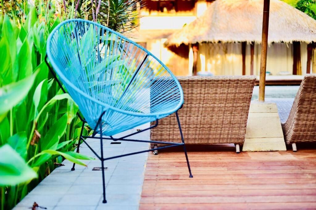 A blue chair and wicker furniture on a wooden deck with a thatched roof structure in the background.