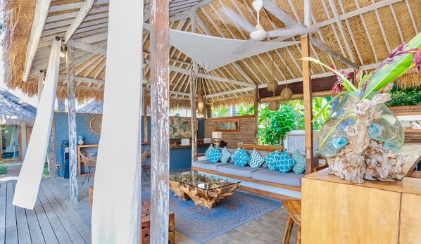 Un salón al aire libre acogedor con terraza de madera, una mesa de centro de vidrio y una zona de estar con cojines.