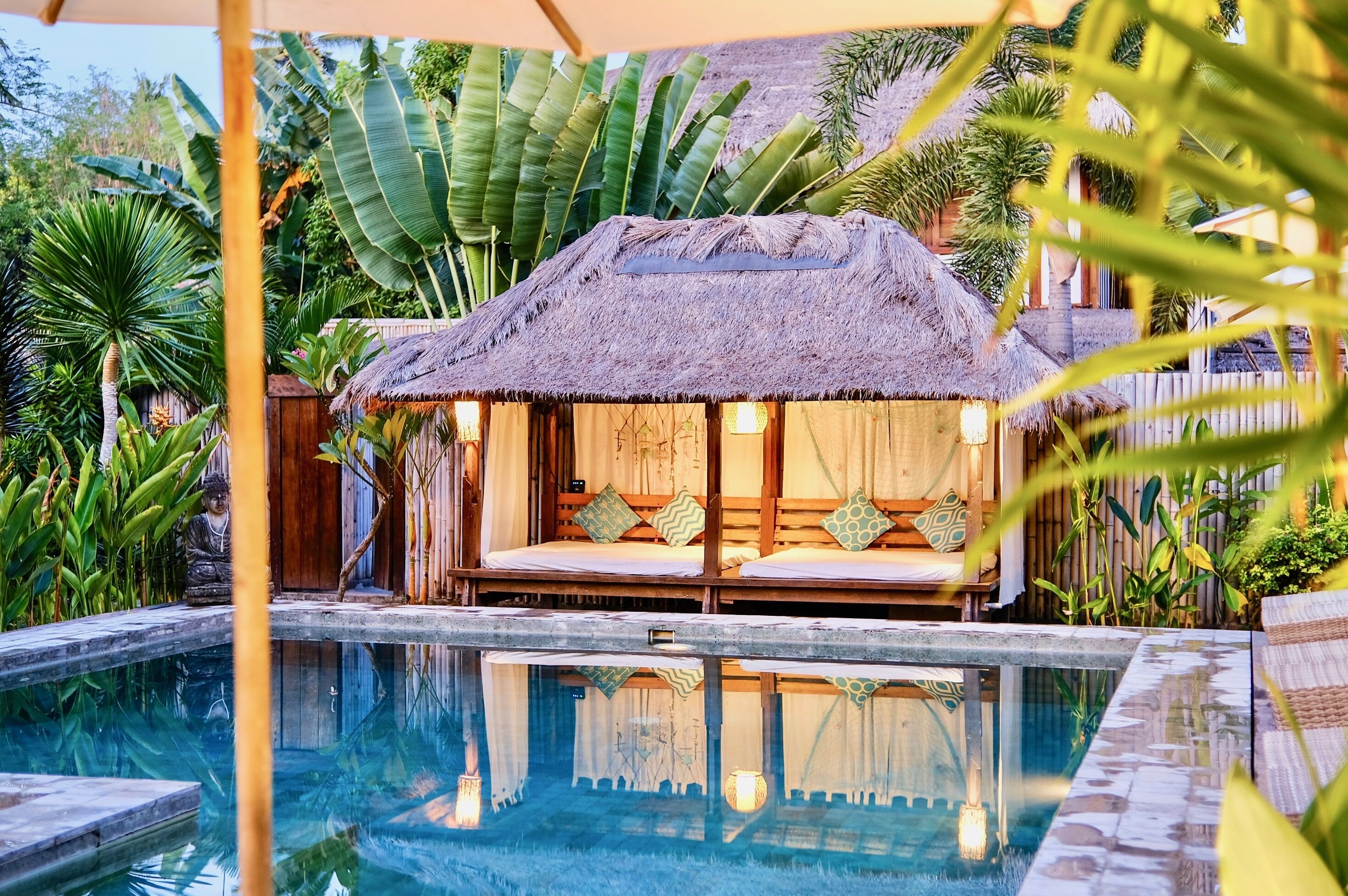 A thatched-roof hut with a bed and a small pool in front.