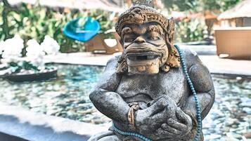 A stone statue of a seated figure with a beaded necklace, positioned by a body of water.