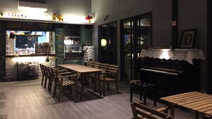 A restaurant with wooden tables and chairs, a piano, and a bar area visible through the glass. - True Love Villa (Hengchun)